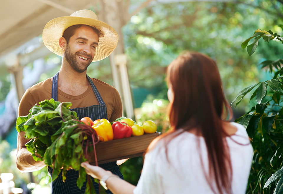 A man in an apron hands a woman a box with fresh produce