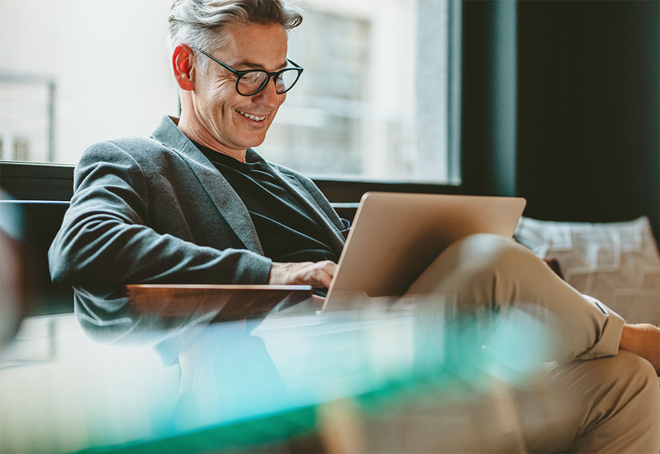 Image of a business man sitting with a laptop computer on his lap. He is working and smiling.