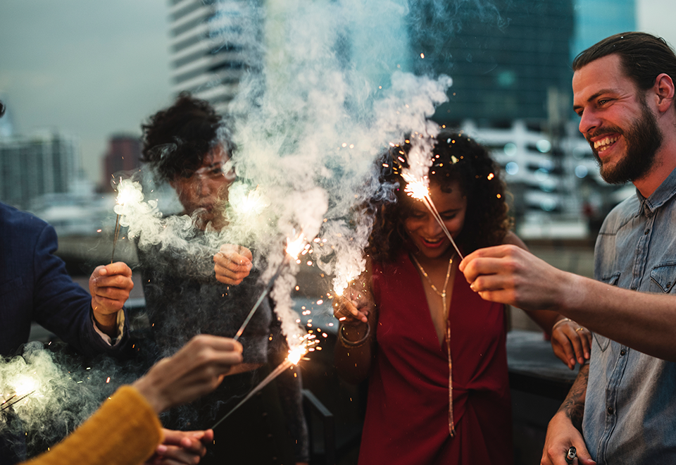 A group of friends stands outside and they are holding sparklers