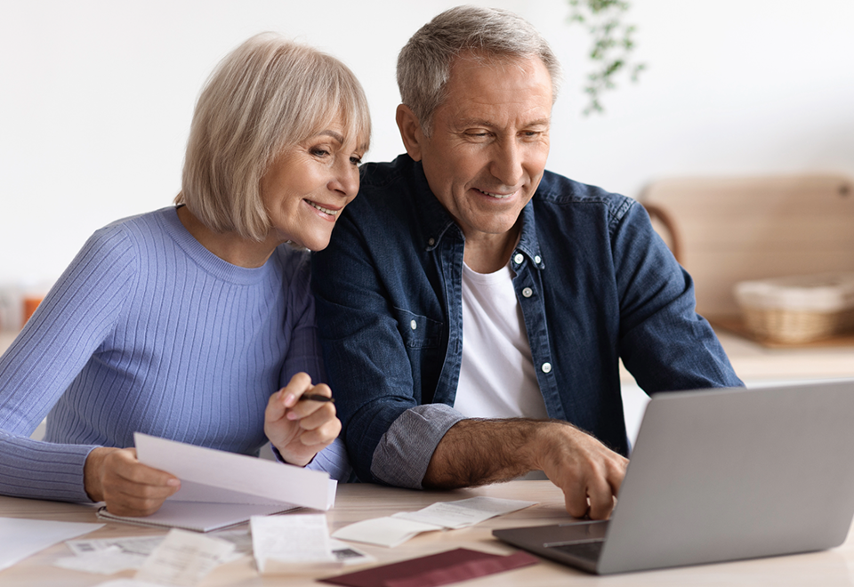 A man and a woman sit at a table, working together on a laptop computer