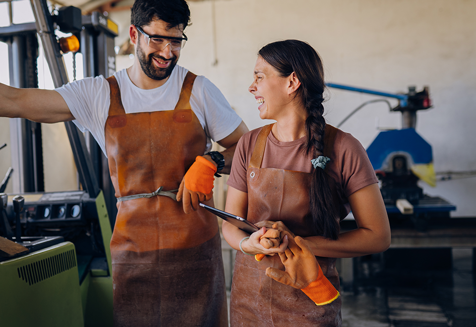 A man and woman in aprons stand next to each other. She is holding a tablet