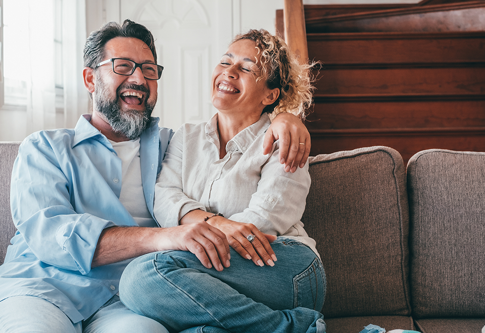 A man and woman sit closely on the couch laughing