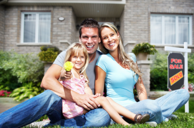 Photo of a mom, dad, and their child seated outside of their house, smiling