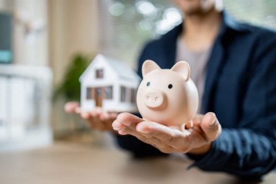 Person holds piggy bank and house model symbolizing savings