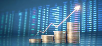 Stacks of coins increasing in height with a rising line chart, symbolizing financial growth against a blue stock-market background.