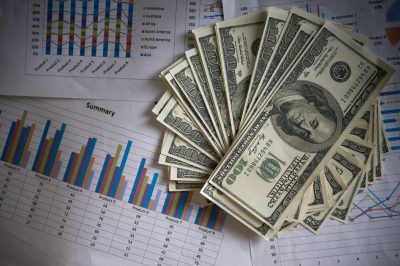 Stacks of $100 bills fanned over printed financial charts and a 'Summary' table, representing cash and business data insights.