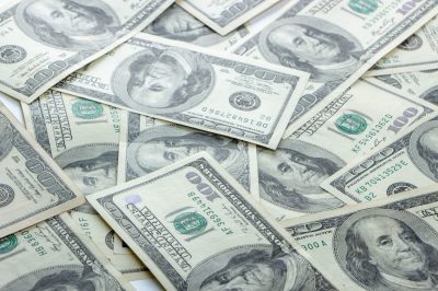 Pile of overlapping US $100 bills spread across a surface, showing Benjamin Franklin’s portrait on many notes.