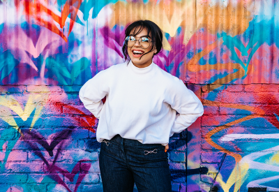 A woman is standing in front of a graffiti'd wall