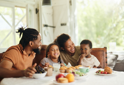 A family of four - two parents and two young children, sit at their table with breakfast in front of them