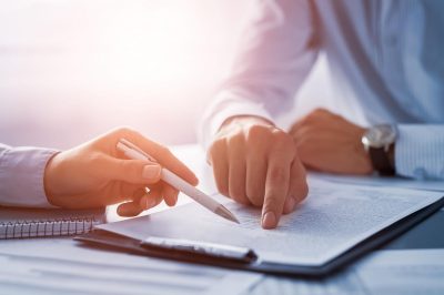 Close of up hands, one hand is holding a pen pointing to a particular place in the paperwork